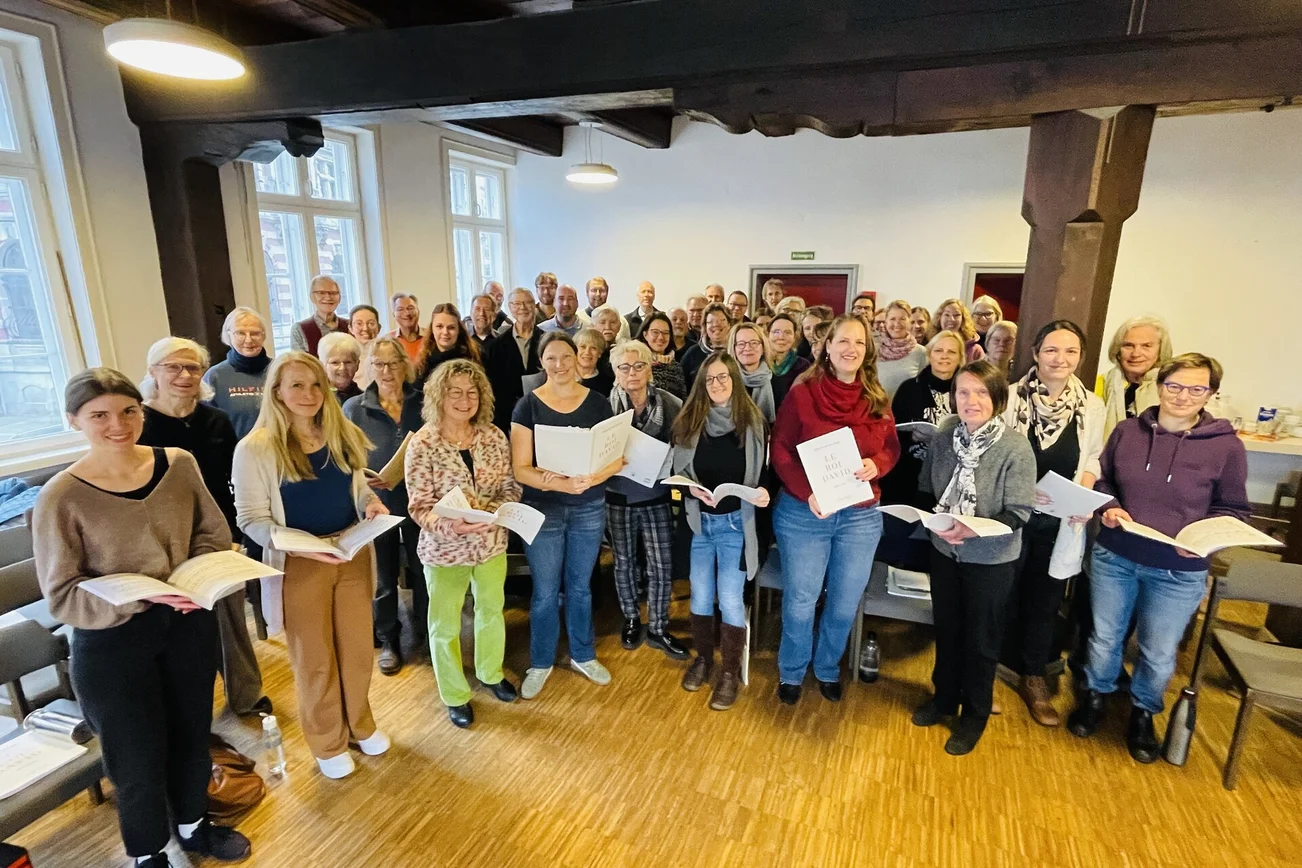 Viele Menschen mit Notenbüchern in den Händen schauen freundlich zur Kamera.