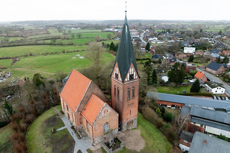 Der Turm der Kirche Sandesneben ragt in den weißen Himmel Das Kirchengebäude links neben dem Turm und rechts die Häuser von Sandesneben - Copyright: Oliver Beck