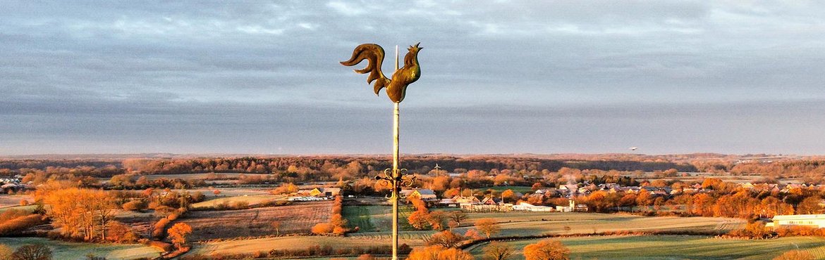 Der Turmhahn ragt in den Himmel und man sieht eine herbstliche Landschaft 