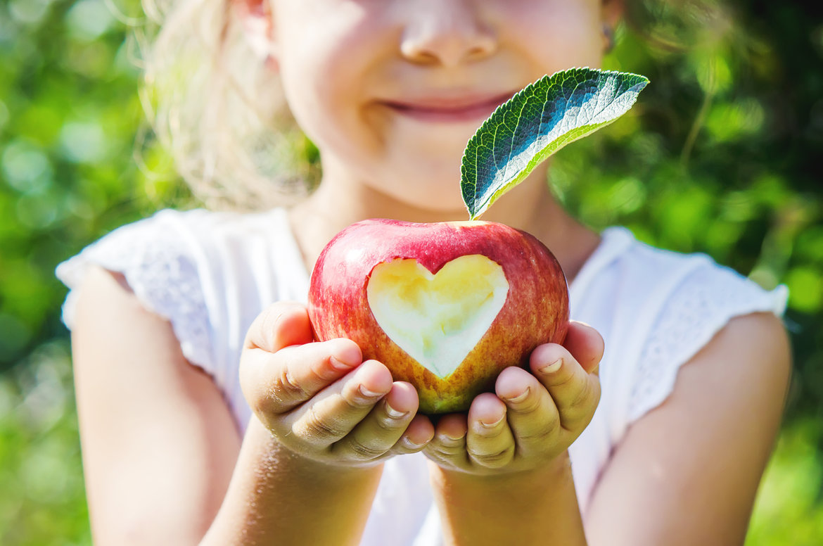 Das Bild zeigt ein Mädchen, das einen Apfel mit einem eingeritzten Herz in ihren Händen hält. 